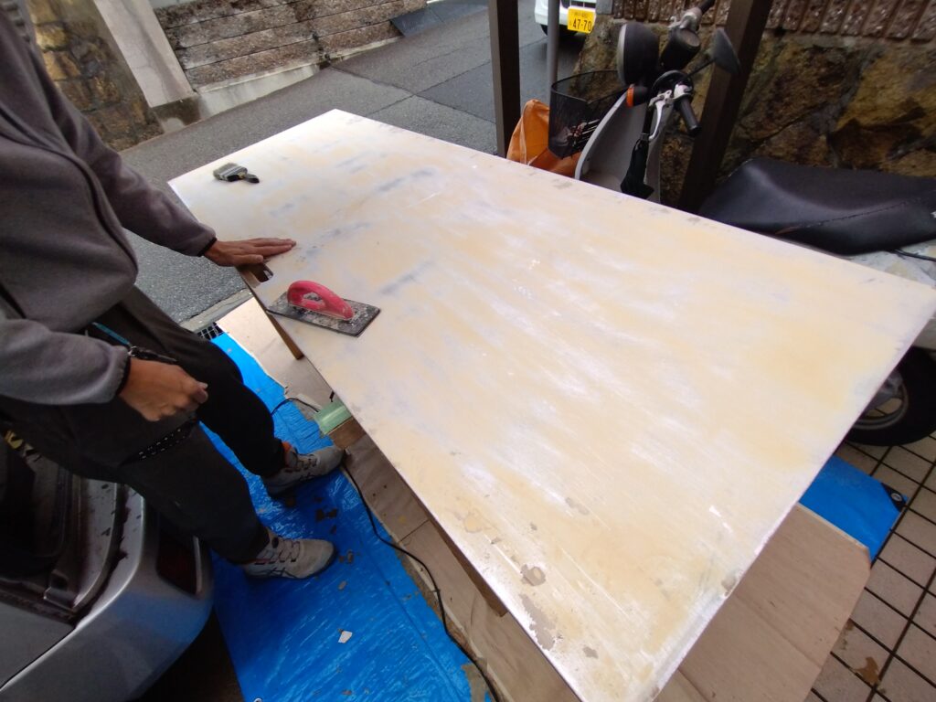 室内ドアの既存化粧シートをスクレーパーで剥がし、パテ処理とペーパー掛けを行っている下地処理工程